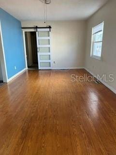 unfurnished room featuring baseboards, a barn door, and wood finished floors