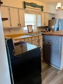 kitchen with stainless steel refrigerator with ice dispenser, light countertops, black electric range oven, and light wood-type flooring
