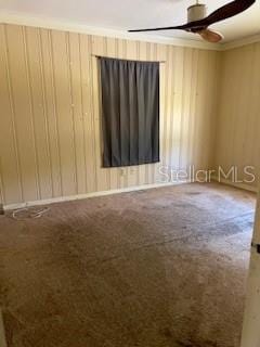 carpeted spare room with ceiling fan and wood walls