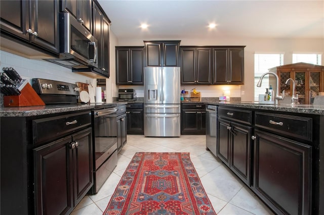 kitchen featuring dark stone counters, light tile patterned flooring, appliances with stainless steel finishes, and a sink