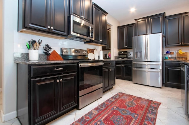 kitchen featuring tasteful backsplash, dark cabinets, dark stone countertops, light tile patterned floors, and stainless steel appliances