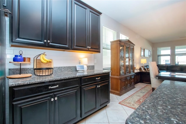 kitchen featuring dark stone counters, dark cabinets, decorative backsplash, and light tile patterned floors