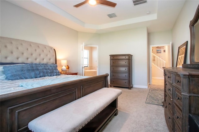 bedroom featuring visible vents, ensuite bathroom, a tray ceiling, and light carpet