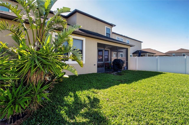 rear view of property with a yard, fence, a sunroom, and stucco siding