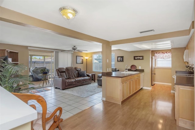 kitchen with visible vents, dark countertops, a sink, light brown cabinets, and white appliances