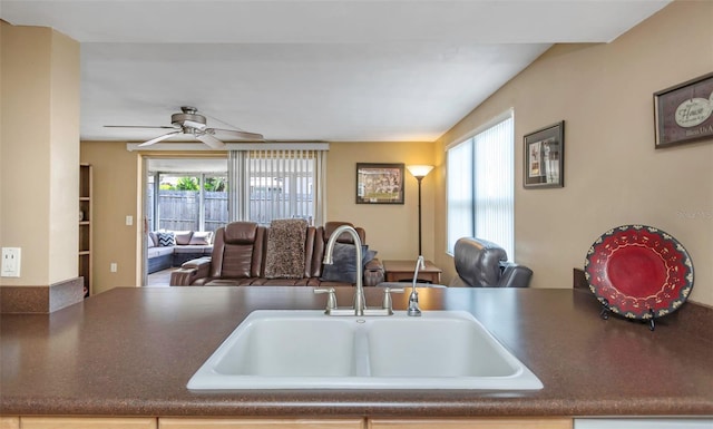 kitchen featuring open floor plan, ceiling fan, dark countertops, and a sink