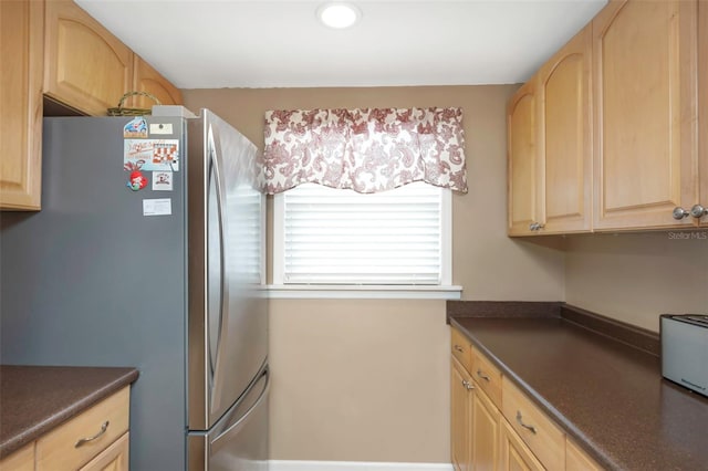 kitchen featuring freestanding refrigerator, light brown cabinetry, dark countertops, and a toaster