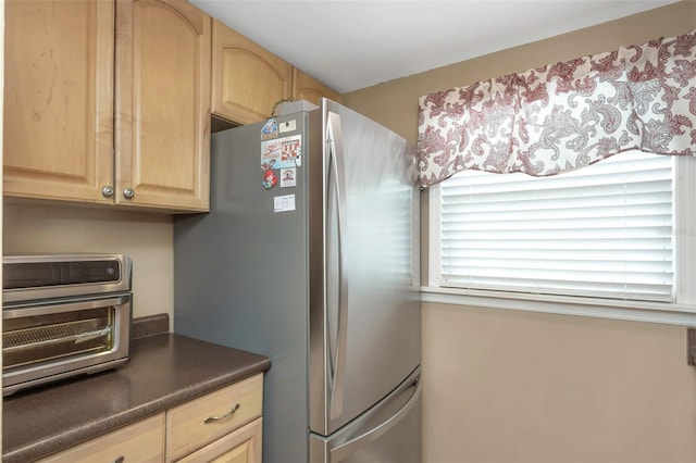 kitchen with freestanding refrigerator, a toaster, light brown cabinets, and dark countertops