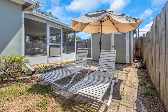 view of patio featuring a sunroom, a fenced backyard, a shed, and an outbuilding