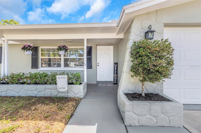 entrance to property with covered porch, stucco siding, and a garage