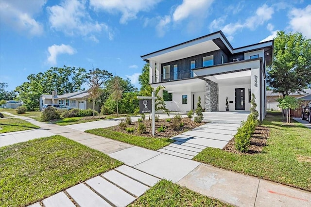 contemporary house with a front lawn, stucco siding, a balcony, and covered porch