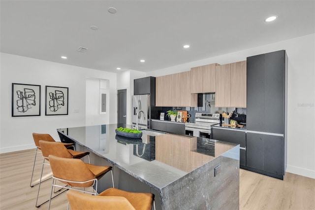kitchen with light wood-style floors, a kitchen breakfast bar, modern cabinets, a center island with sink, and stainless steel appliances