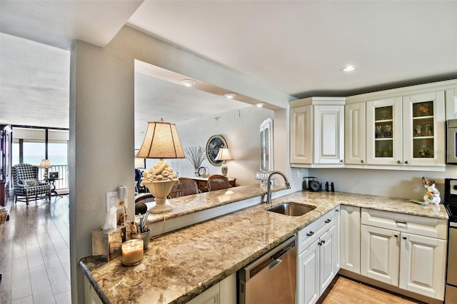 kitchen with glass insert cabinets, light wood-style flooring, a sink, stainless steel dishwasher, and light stone counters