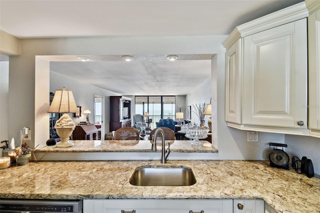 kitchen featuring dishwashing machine, light stone countertops, open floor plan, and a sink