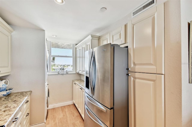 kitchen featuring stainless steel fridge with ice dispenser, light wood-type flooring, visible vents, baseboards, and light stone counters