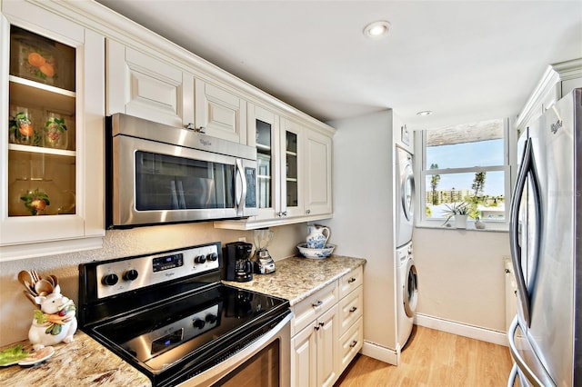 kitchen featuring stacked washer and clothes dryer, glass insert cabinets, stainless steel appliances, light wood-type flooring, and baseboards