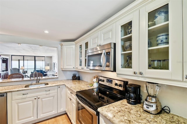 kitchen with a sink, white cabinetry, glass insert cabinets, light stone countertops, and appliances with stainless steel finishes