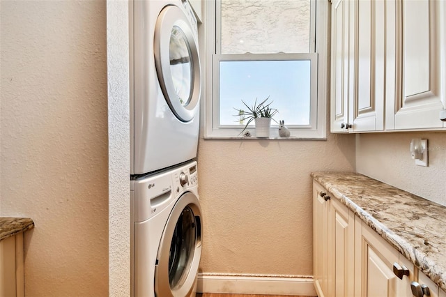 clothes washing area with stacked washer and dryer, a textured wall, and cabinet space