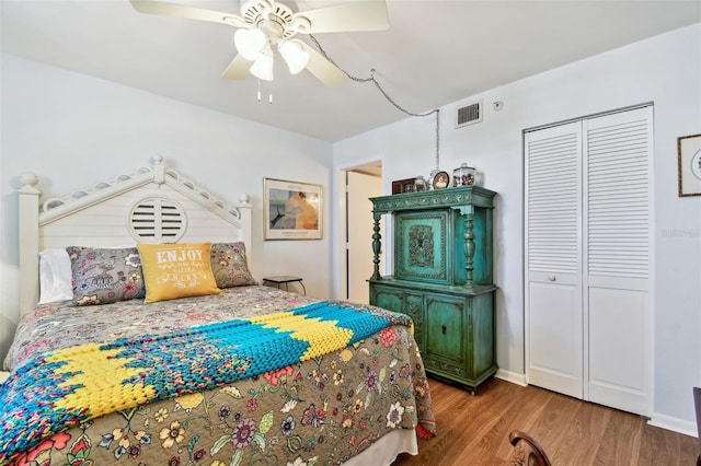 bedroom with a closet, wood finished floors, visible vents, ceiling fan, and baseboards