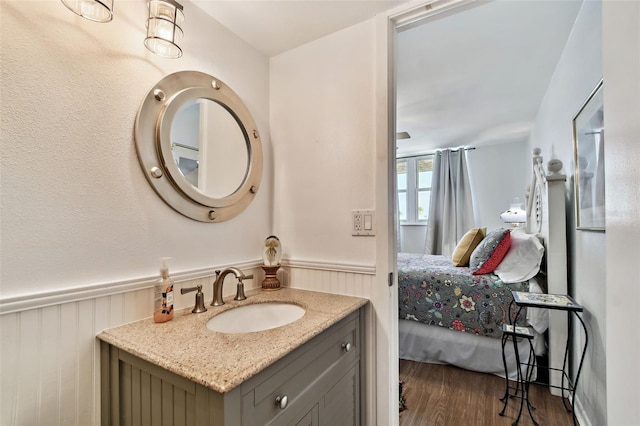 ensuite bathroom with connected bathroom, vanity, wood finished floors, and a wainscoted wall