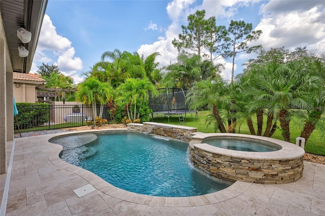 view of swimming pool featuring a pool with connected hot tub, fence, and a trampoline