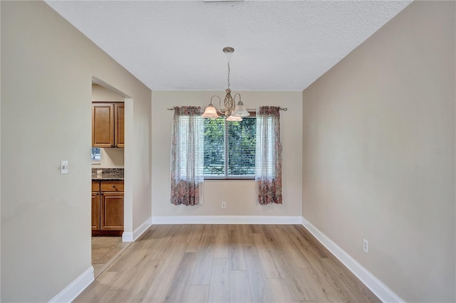 2961 Briar Cliff Dr, Palm Harbor, FL 34684 - unfurnished dining area with an inviting chandelier, baseboards, light wood finished floors, and a textured ceiling