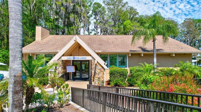 2961 Briar Cliff Dr, Palm Harbor, FL 34684 - view of front facade featuring fence, french doors, roof with shingles, and stucco siding
