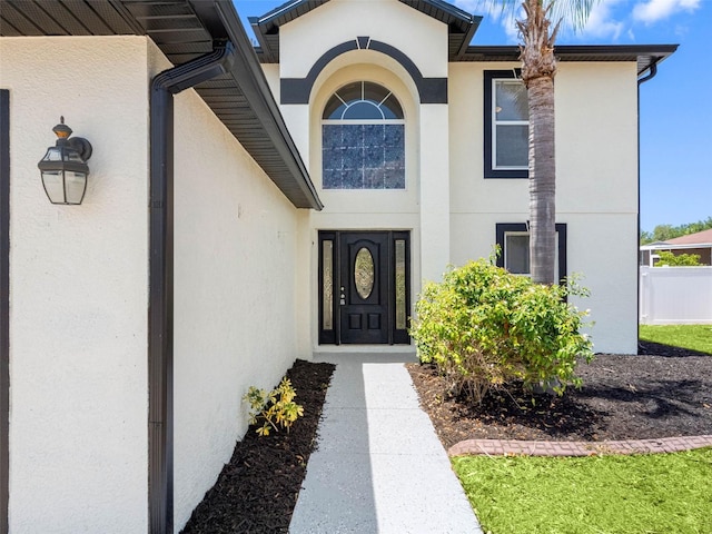view of exterior entry featuring stucco siding and fence