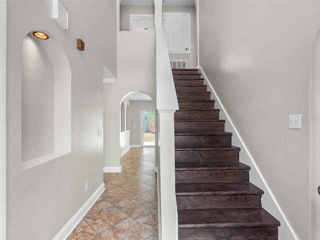 staircase with a towering ceiling, visible vents, arched walkways, tile patterned flooring, and baseboards