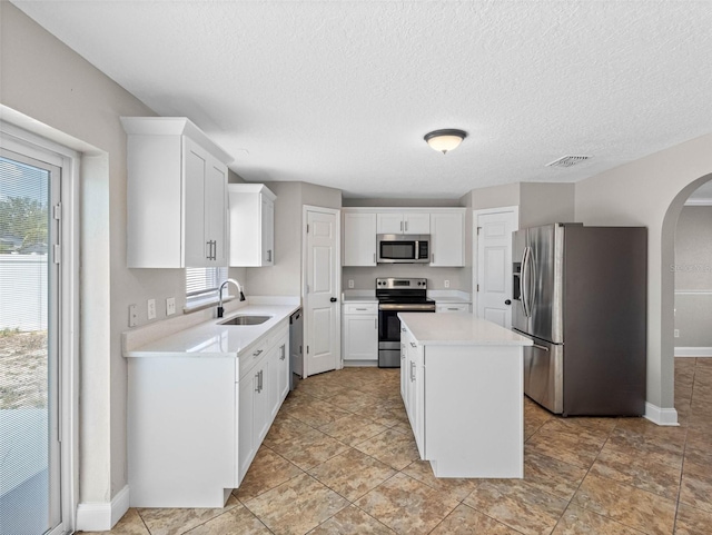 kitchen featuring appliances with stainless steel finishes, a sink, arched walkways, a kitchen island, and visible vents