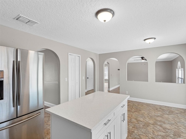 kitchen with white cabinets, ceiling fan, stainless steel fridge with ice dispenser, a center island, and visible vents