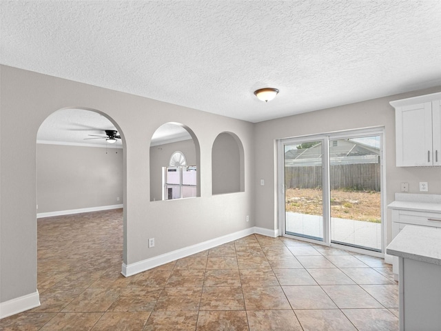 unfurnished dining area with baseboards, a ceiling fan, and a textured ceiling