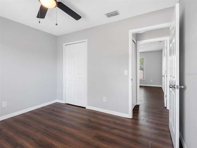 unfurnished bedroom with a closet, baseboards, dark wood-type flooring, and visible vents