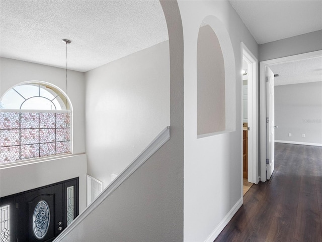 hallway with baseboards, arched walkways, a textured ceiling, and wood finished floors