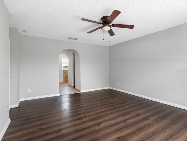 empty room featuring visible vents, wood finished floors, baseboards, ceiling fan, and arched walkways