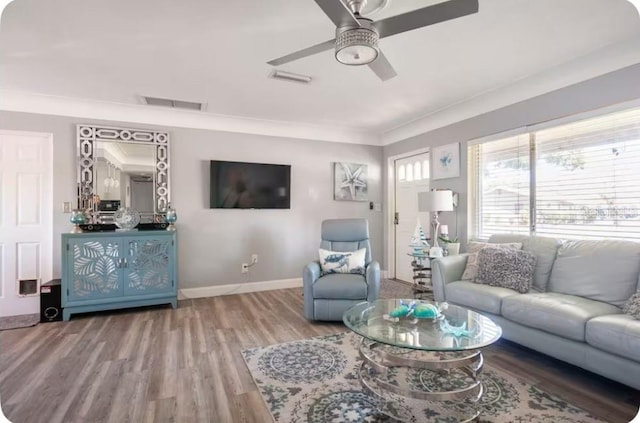 living area with a ceiling fan, baseboards, wood finished floors, visible vents, and ornamental molding
