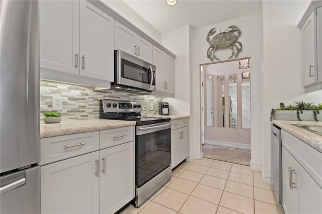 7 Island Park Pl Unit 204, Dunedin, FL 34698 - kitchen with stainless steel appliances, decorative backsplash, light tile patterned floors, baseboards, and white cabinetry
