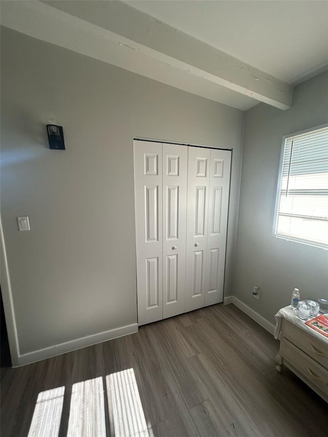 unfurnished bedroom with baseboards, beam ceiling, a closet, and wood finished floors