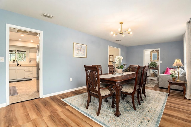 dining room with a chandelier, light wood-style flooring, and baseboards