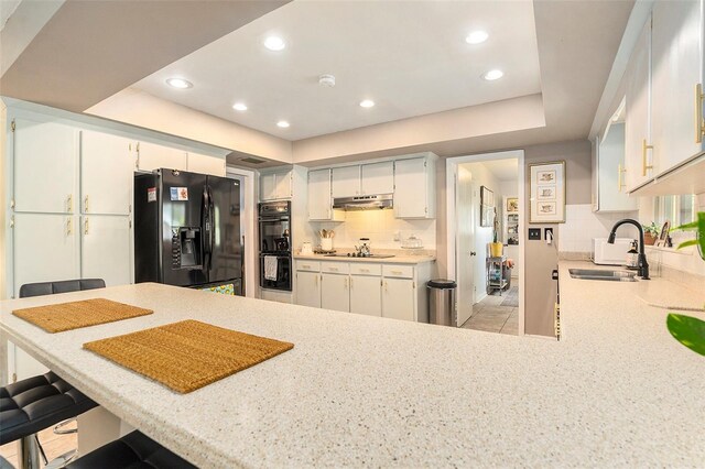 kitchen with black appliances, a sink, under cabinet range hood, decorative backsplash, and light countertops