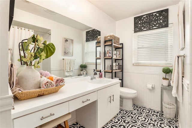 full bath featuring toilet, wainscoting, and vanity