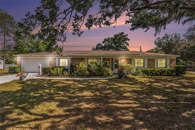 ranch-style house featuring a yard, driveway, an attached garage, and brick siding