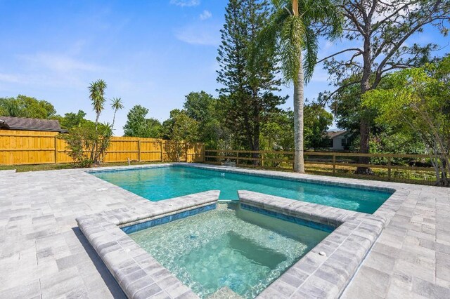 view of pool with a fenced backyard, a pool with connected hot tub, and a patio area
