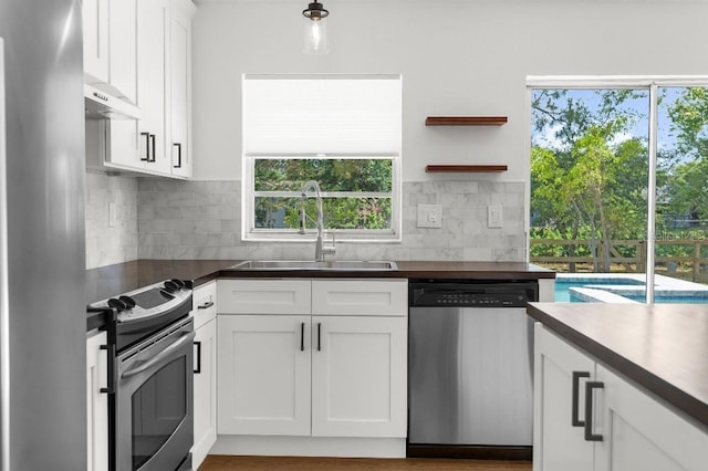 kitchen featuring stainless steel appliances, dark countertops, white cabinetry, and a sink