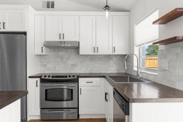 kitchen featuring open shelves, dark countertops, under cabinet range hood, a sink, and stainless steel appliances