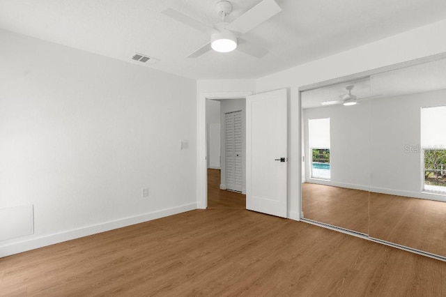 unfurnished bedroom featuring visible vents, a closet, wood finished floors, baseboards, and ceiling fan