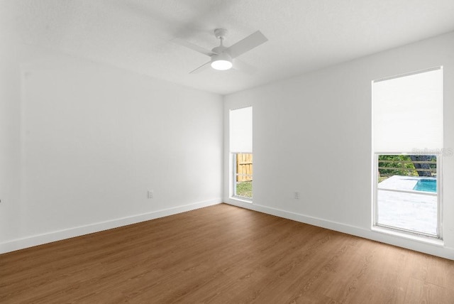 spare room featuring baseboards, ceiling fan, a healthy amount of sunlight, and wood finished floors