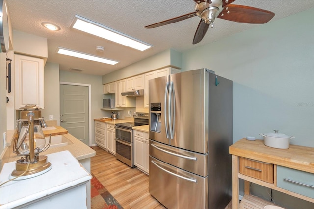 kitchen featuring appliances with stainless steel finishes, light countertops, a ceiling fan, light wood-style flooring, and a textured ceiling