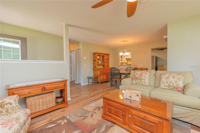 living area featuring a ceiling fan, light wood-style floors, and a chandelier