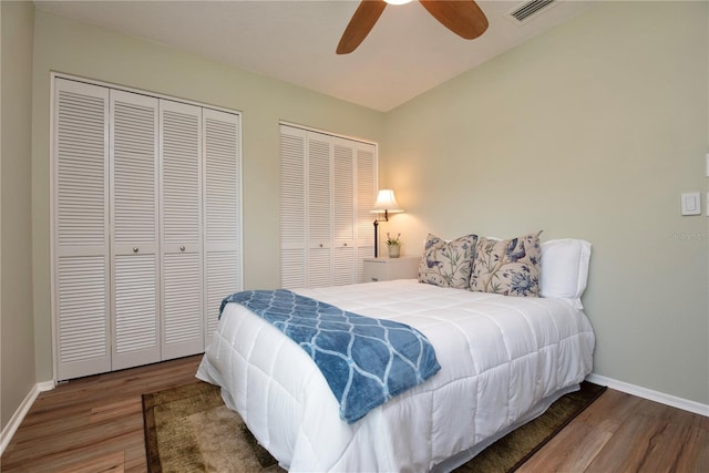 bedroom with wood finished floors, baseboards, multiple closets, and ceiling fan